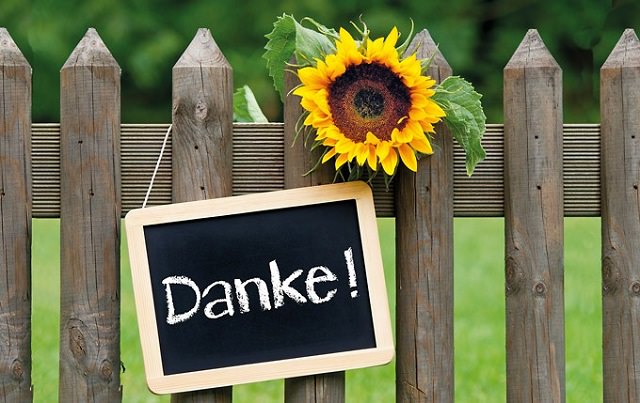 Schiefertafel mit Aufschrift "Danke" über einem Gartenzaun hängend.