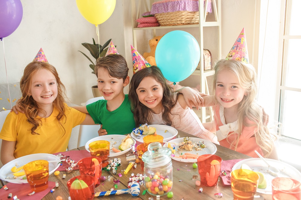 Feiernde Kinder sitzen bei der Geburtstagsparty um den Tisch