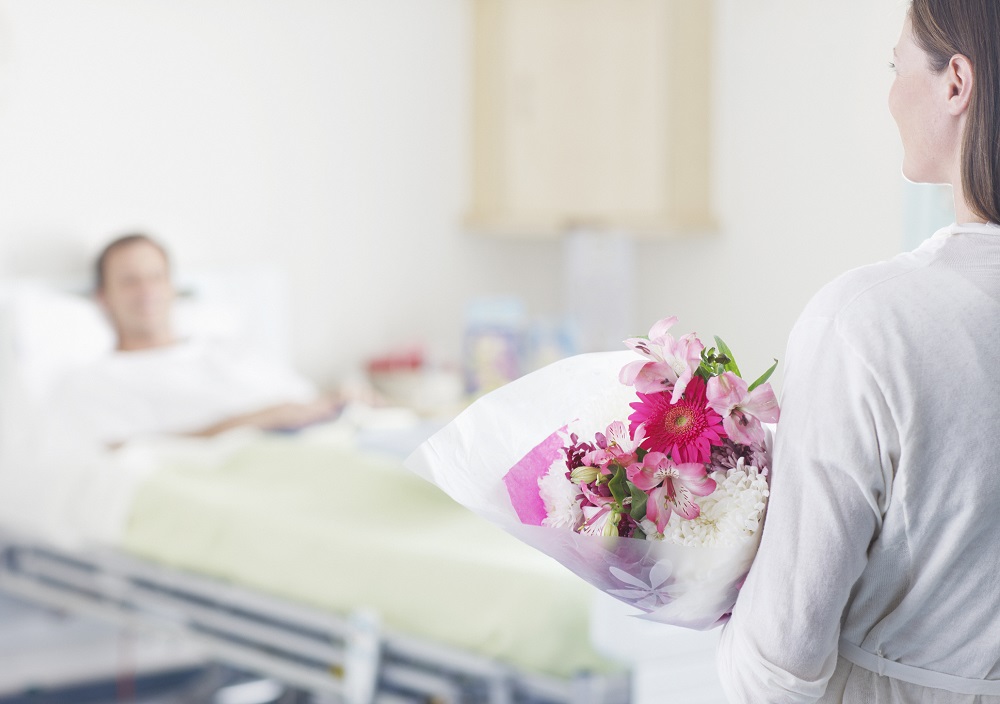 Frau mit Blumen zu Besuch im Krankenhaus bei krankem Kollegen 