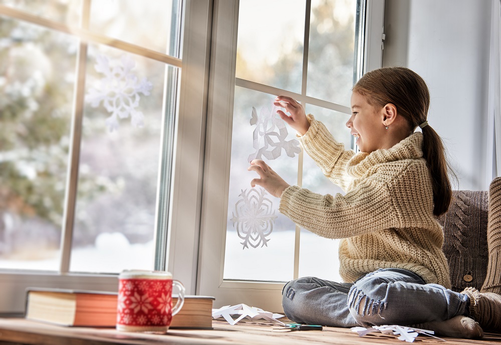Kind hilft beim weihnachtlichen Dekorieren der Fenster.