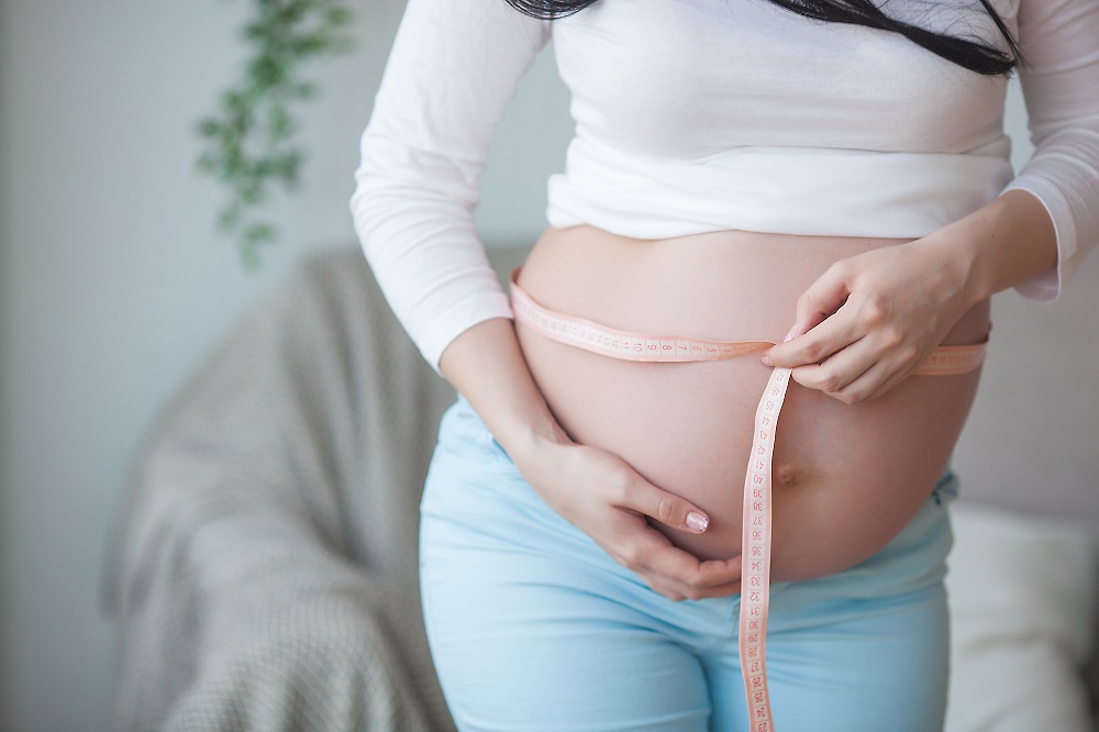 Schwangere misst Babybauch mit Maßband