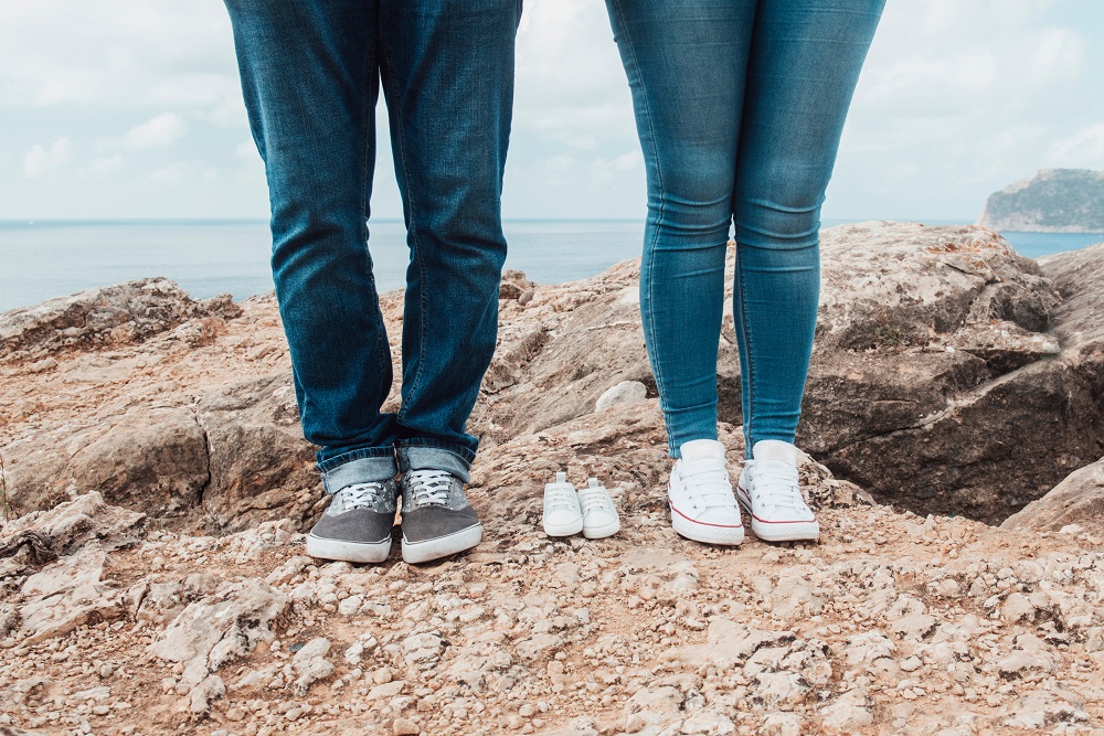 Mann und Frau stehen nebeneinander, zwischen ihnen liegt ein paar Babyschuhe