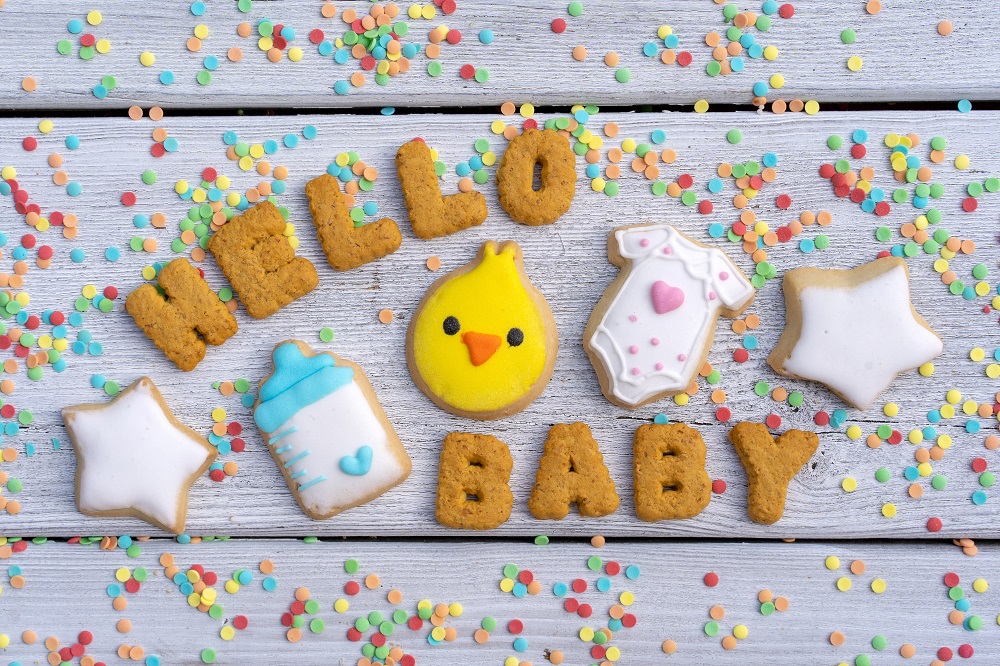 Schriftzug "Hello Baby" aus Keksen gebacken liegt auf einem Tisch mit Konfetti