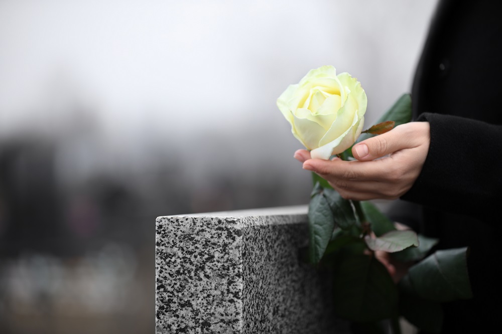 weiße Rose in der Hand einer trauernden Person