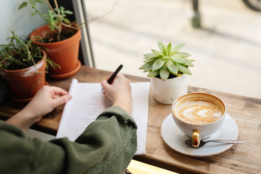 Frau schreibt in Notizheft und trinkt Kaffee